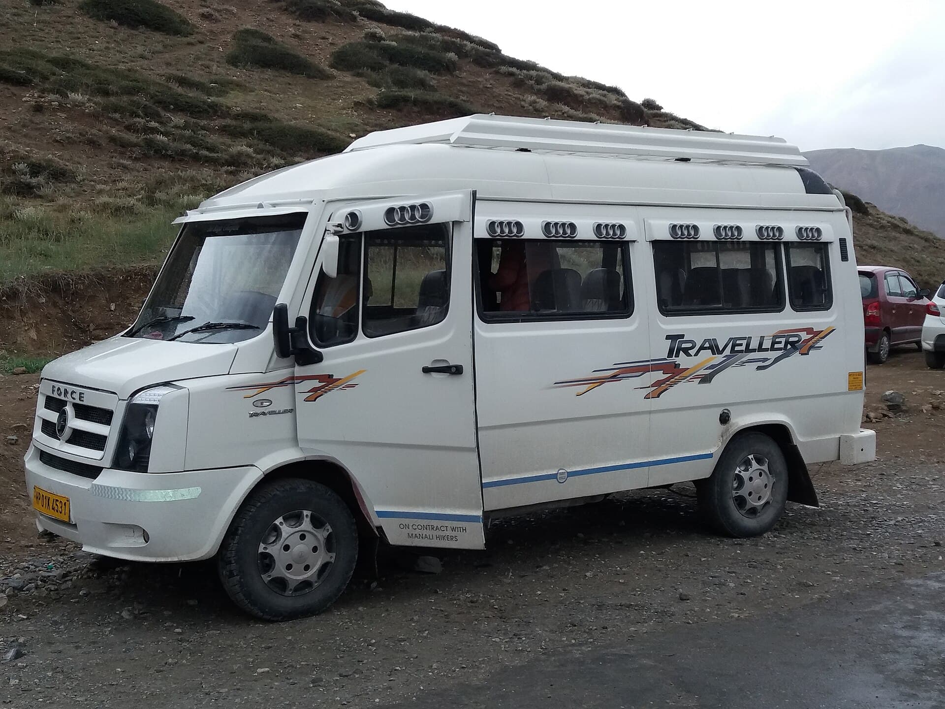White Force Traveller tempo traveller van, front three-quarter view, parked beside the Leh-Manali Highway