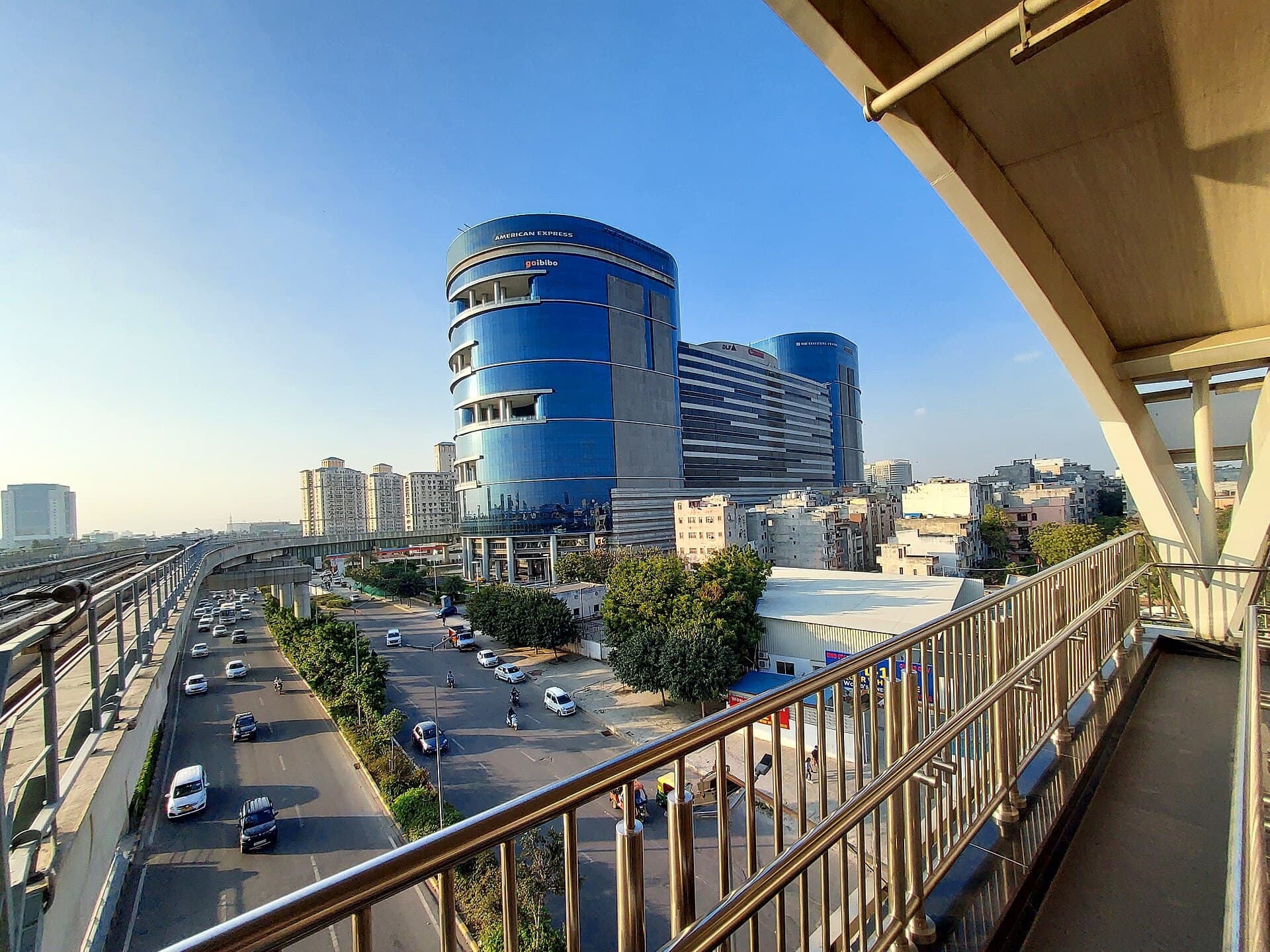Glass office towers in DLF Phase 3, Gurugram, seen from a metro walkway above a busy road